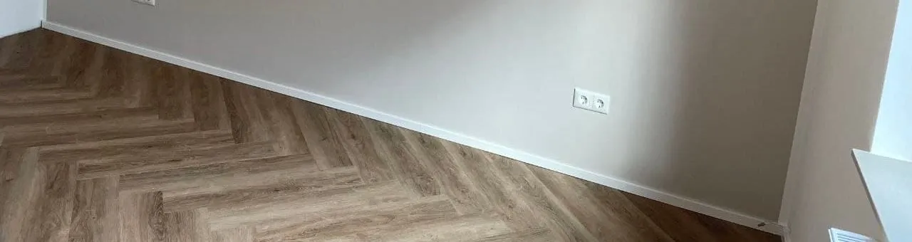 Vinylboden trifft in einer sauberen Linie auf die fertige Wand, dahinter die Sockelkante